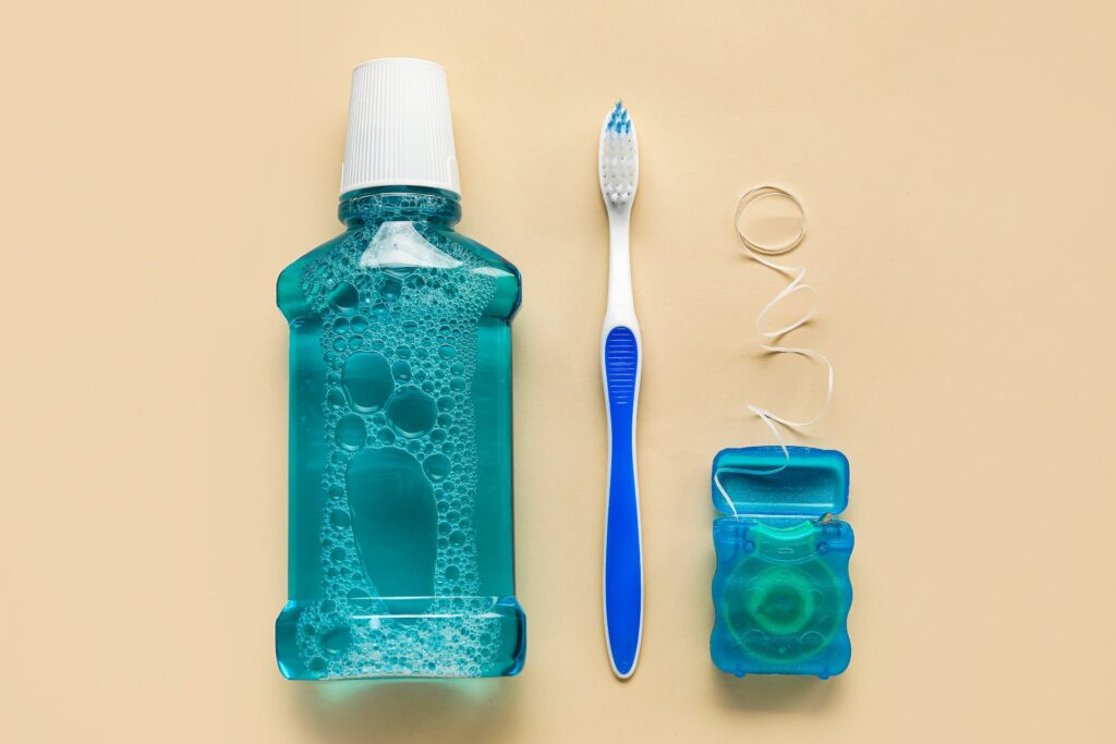 Mouthwash, toothbrush, and dental floss against a light yellow background.