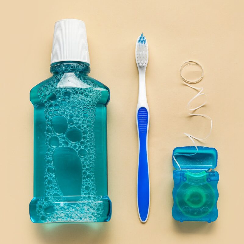 Mouthwash, toothbrush, and dental floss against a light yellow background.